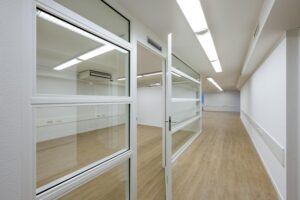 Leeg kantoorpand aan de Prins Hendrikkade met glazen binnenwanden en houten vloer.